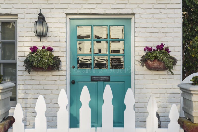 Teal front door of a classic home. A teal wooden front door to a home, with white picket fence gate in foreground. The door is framed by two flower planters, and royalty free stock photography